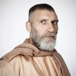 Белорусские ученые раскритиковали реконструкцию лица древнего человека, который жил под Волковыском Мужчина с бородой и шалью, одетый в одежду нейтральных тонов, смотрит в камеру на однотонном фоне, напоминая древнего человека из Волковыска.