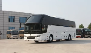 Сучасны белы турыстычны кітайскі аўтобус Zhong Tong прыпаркаваны на бетоннай паверхні каля вялікага будынка.